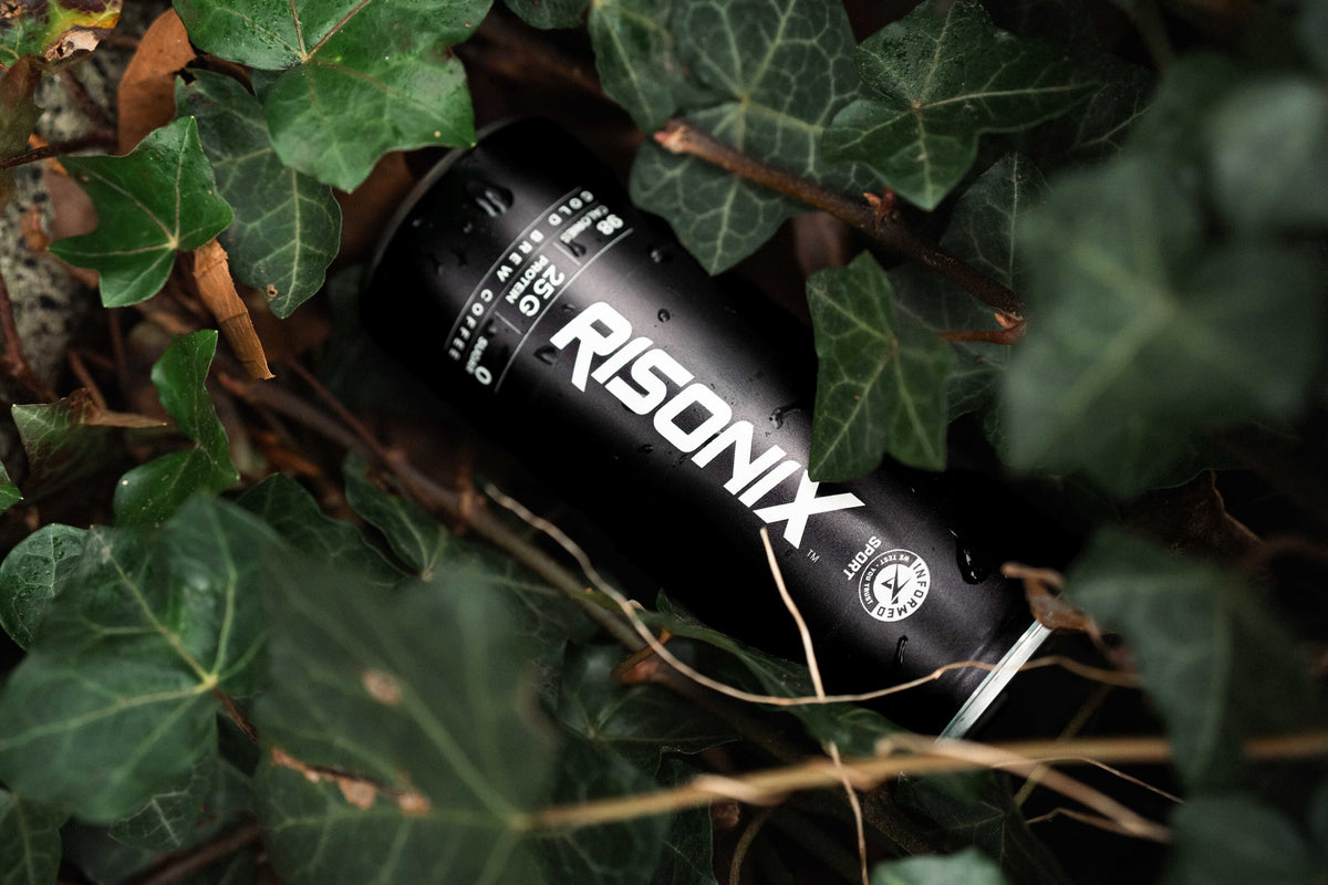 A RISONIX Energy can lying among dark green ivy leaves.