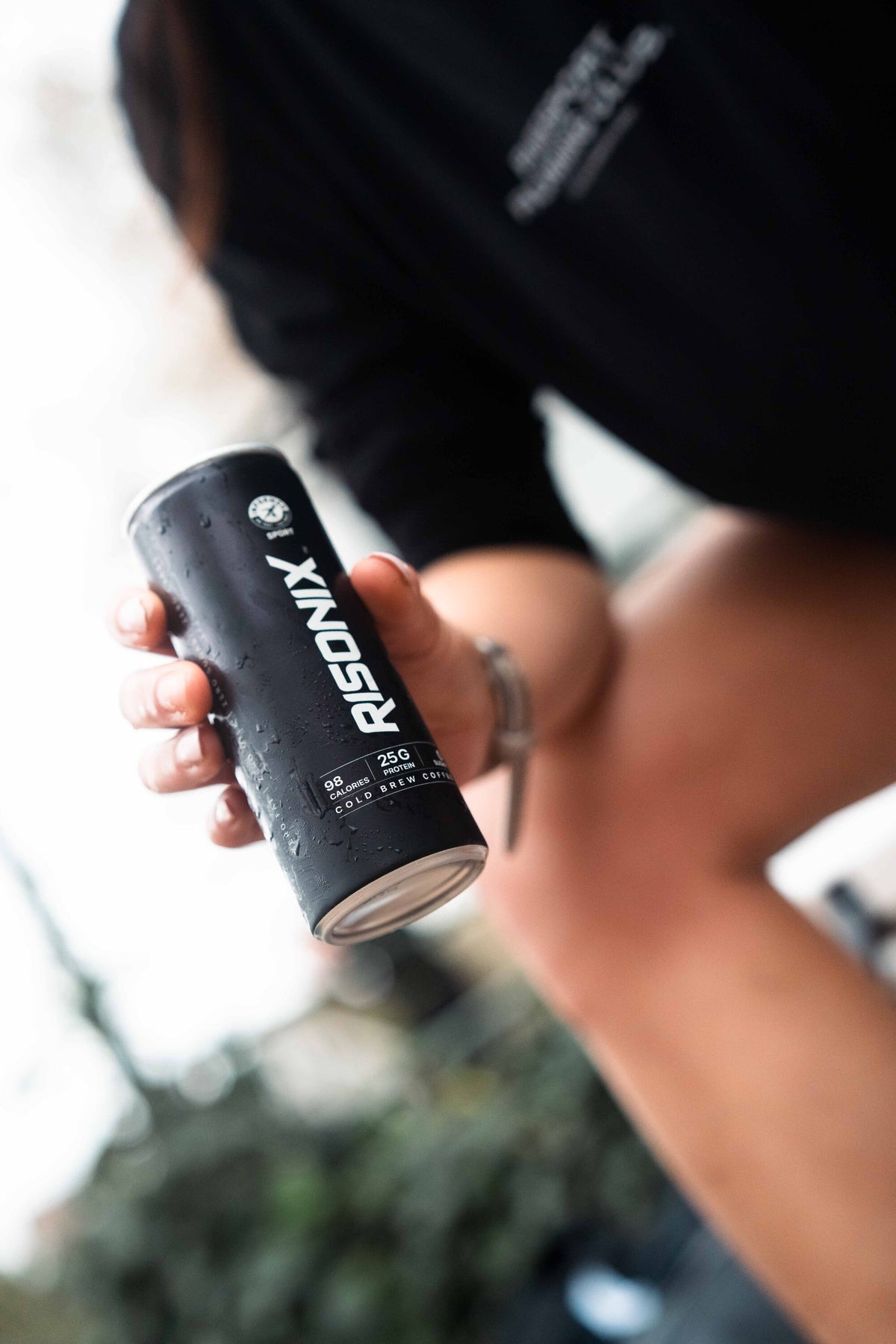 A person outdoors holding a chilled RISONIX Energy can, condensation on the matte black body.