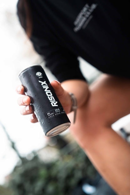 A person outdoors holding a chilled RISONIX Energy can, condensation on the matte black body.